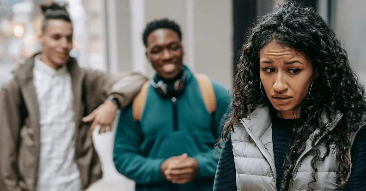 College student experiencing social anxiety while two classmates talk in the background, highlighting social challenges in college.