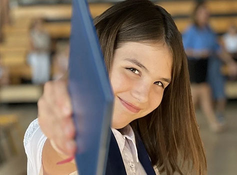 girl pointing a book at the camera smiling after adhd therapy.